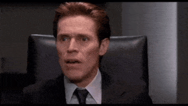a man in a suit and tie is sitting in a chair making a funny face .