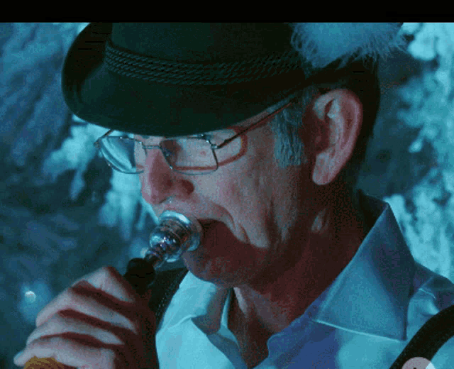 a man wearing glasses and a black hat is drinking from a bottle