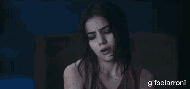 a woman is sitting in a dark room with the words gifselaroni written below her