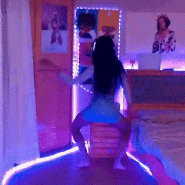 a woman is dancing in a room with purple lights and a bed .