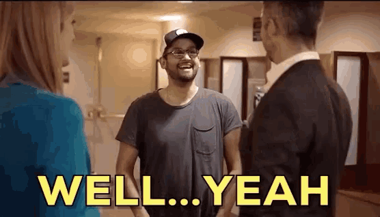 a man in a hat and glasses is laughing while talking to a woman and a man in a suit .