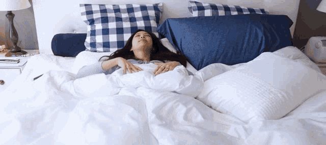 a woman is laying on a bed with white sheets and blue pillows