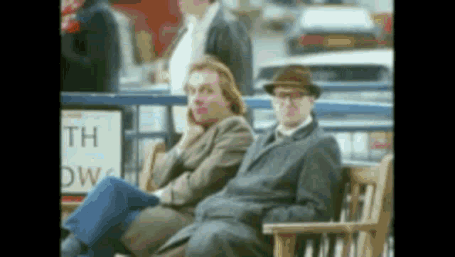 two men are sitting on a bench in front of a sign that says " th "