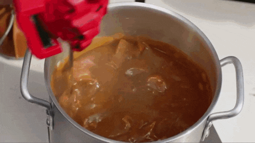 a pot of stew is being stirred with a red glove .