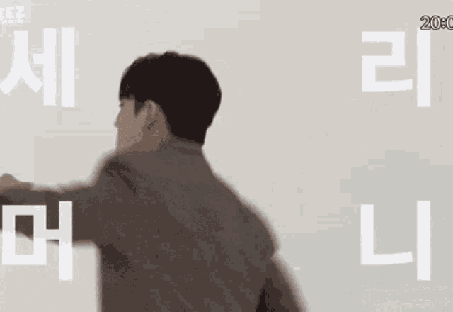 a man in a suit and tie is dancing in front of a wall with korean writing .