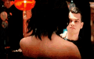 a man and a woman are looking at each other in a dark room with a red lantern in the background