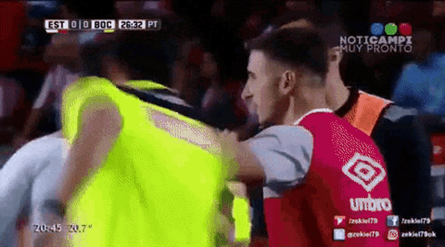 a soccer player wearing a red umbro jersey is hugging another soccer player