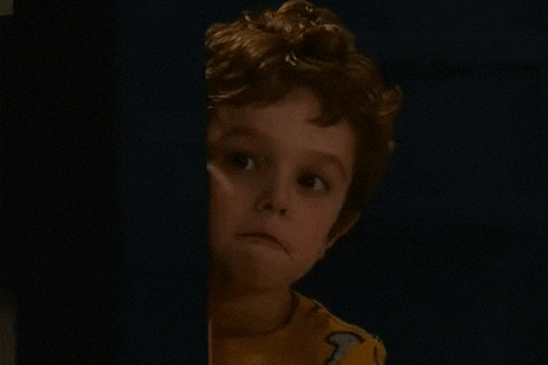 a young boy is peeking out from behind a curtain