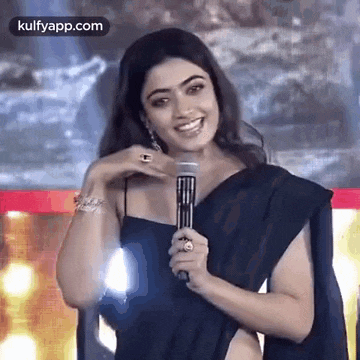 a woman is holding a microphone and smiling while wearing a black saree .