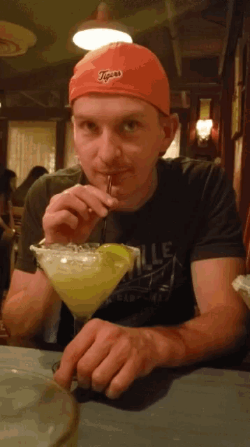 a man wearing an orange tigers hat drinks from a margarita