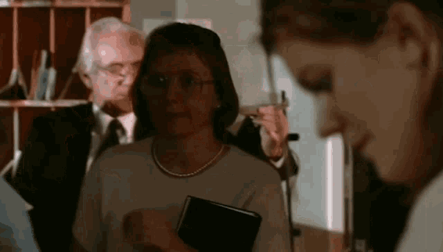 a woman with glasses is holding a black book in her hand