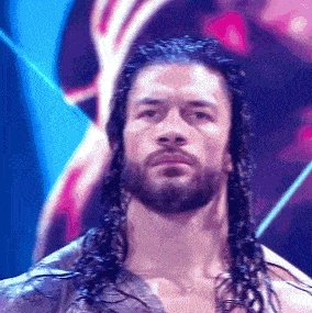 a wrestler with long hair and a beard is standing on a stage .
