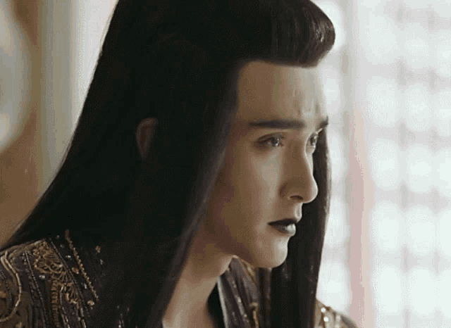 a man with long black hair is wearing a purple and gold robe