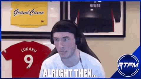 a man wearing headphones is sitting in front of a display of jerseys and says alright then .