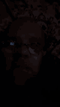 a close up of a person 's face in the dark with a cell phone in the background