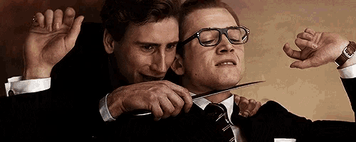 a man in glasses is holding another man 's neck with a knife