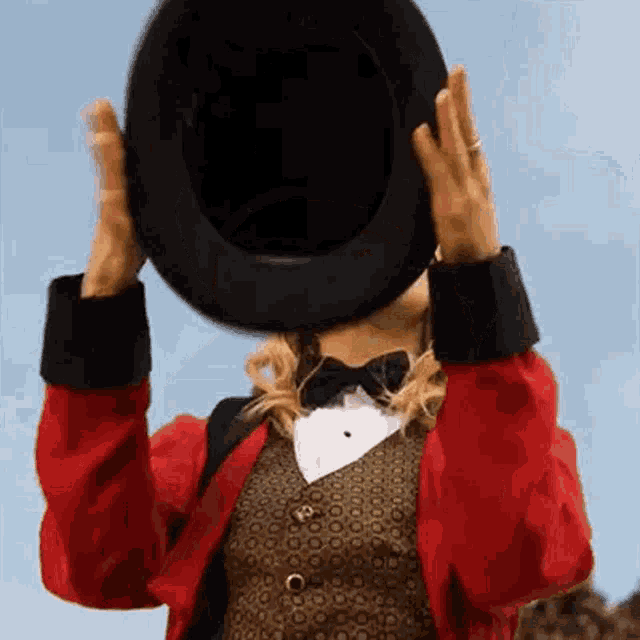a woman in a red jacket and bow tie is holding a black top hat over her head .