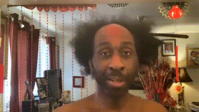 a man with a beard is standing in a living room with red curtains