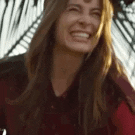 a woman with long hair is smiling and laughing while wearing a red shirt .