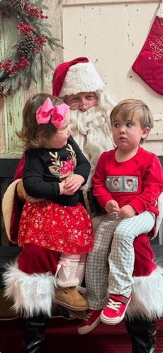 two children are sitting on santa 's lap and one of them is wearing a shirt that says christmas