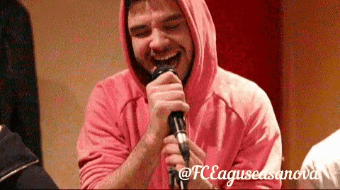 a man wearing a pink hoodie is singing into a microphone ..