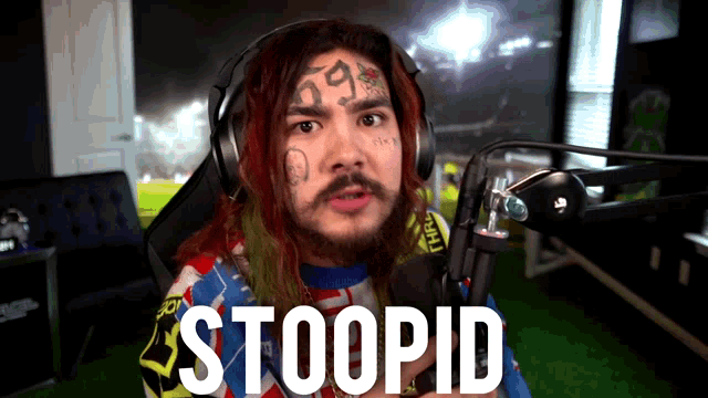 a man with a tattoo on his face is wearing headphones and has the word stoopid on his face
