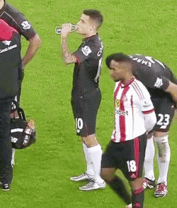 a soccer player with the number 18 on his shorts is drinking from a bottle