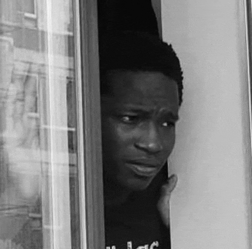 a black and white photo of a man peeking out of a doorway .
