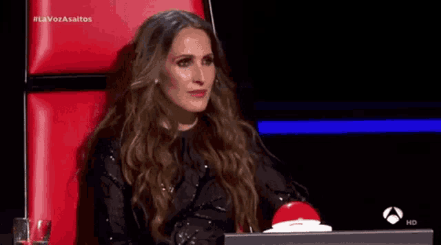 a woman is sitting in a red chair with a red button on the desk .