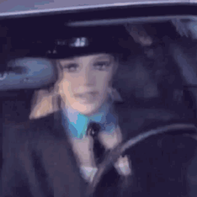 a woman in a police hat is driving a car and looking at the rear view mirror .