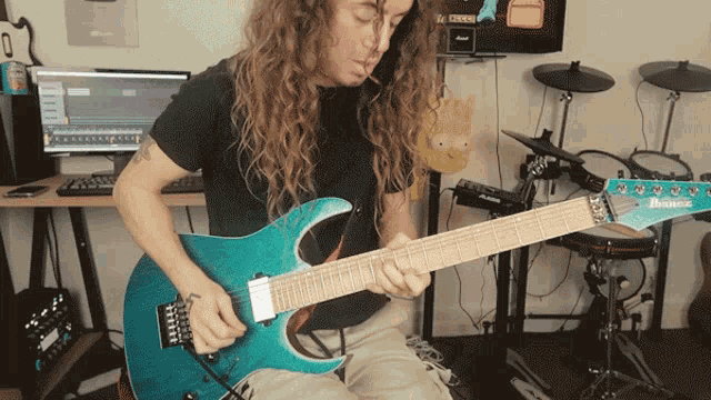a man with long hair is playing a turquoise ibanez guitar