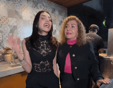 two women are standing next to each other and one of them is wearing a pink sweater