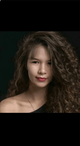 a woman with long curly hair is wearing a black top and red lipstick