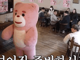 a pink teddy bear is standing in front of a group of people sitting at tables ..