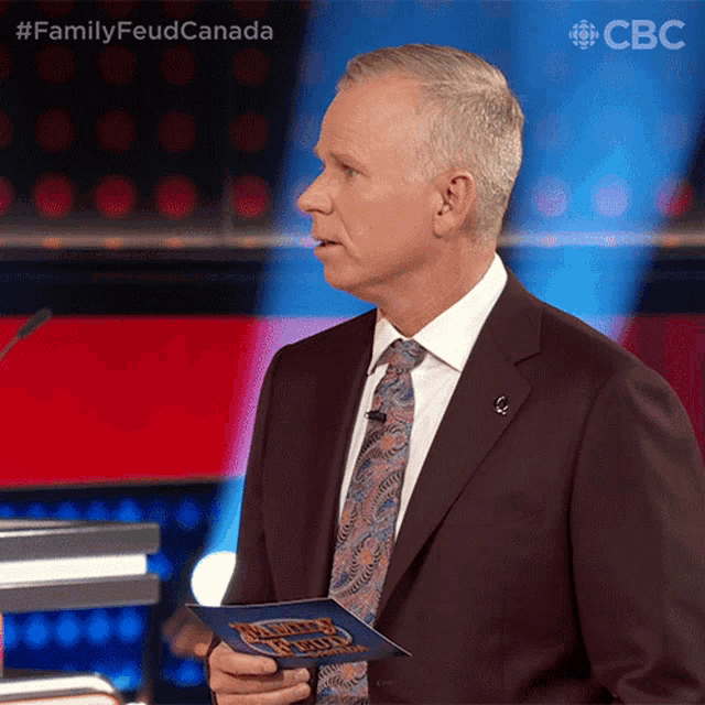 a man in a suit and tie stands in front of a microphone holding a piece of paper that says family feud
