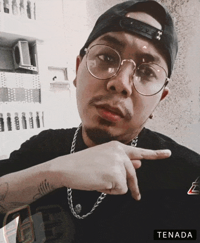 a man wearing glasses and a hat is pointing at the camera with the word tenada below him