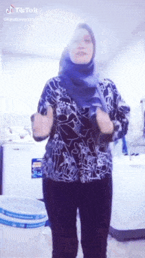 a woman wearing a blue hijab is standing in front of a washing machine .