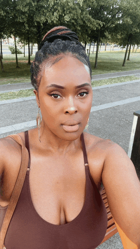 a woman in a brown top is taking a selfie in a park