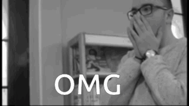 a man with glasses is covering his face with his hands and the word omg is on the screen