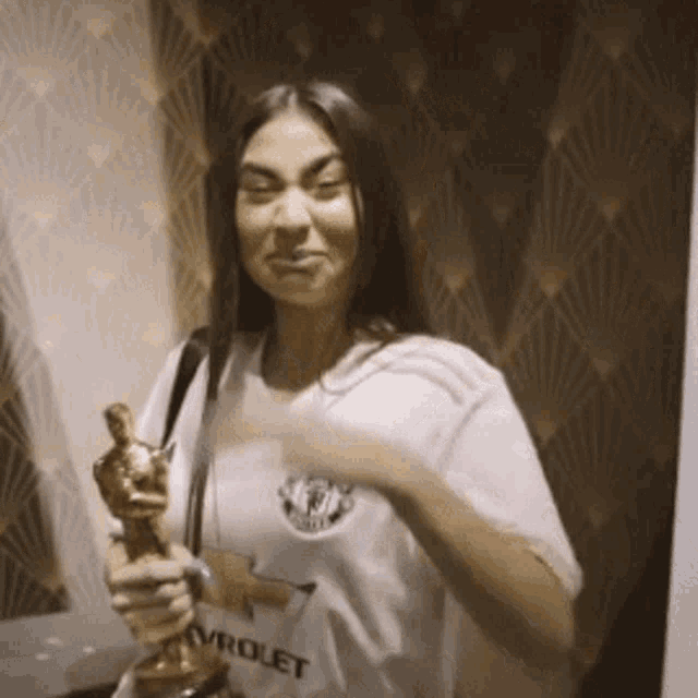 a woman in a chevrolet shirt is holding an oscar trophy
