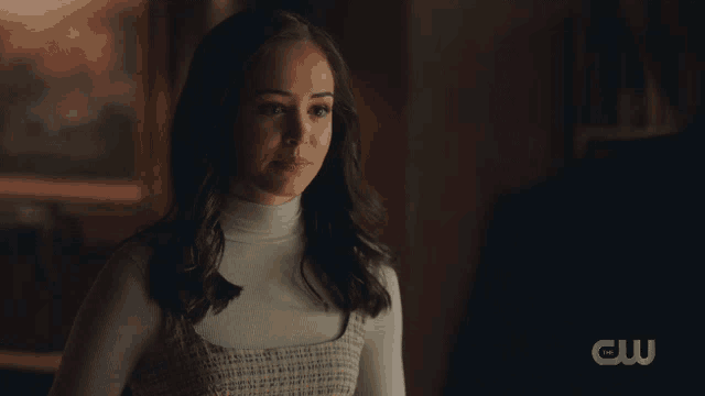 a woman in a white turtleneck and plaid dress stands in a dark room