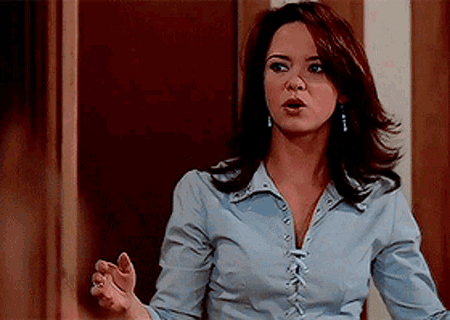 a woman wearing a blue shirt and earrings is making a funny face