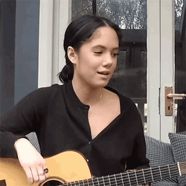 a woman in a black shirt is playing a guitar .