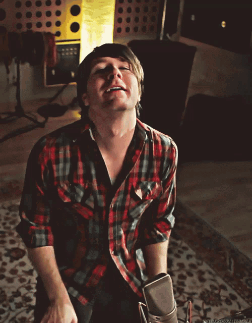 a man in a plaid shirt is smiling while sitting on the floor