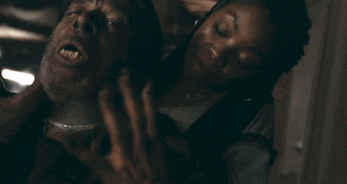 a woman is holding a man 's neck while he screams with his mouth open