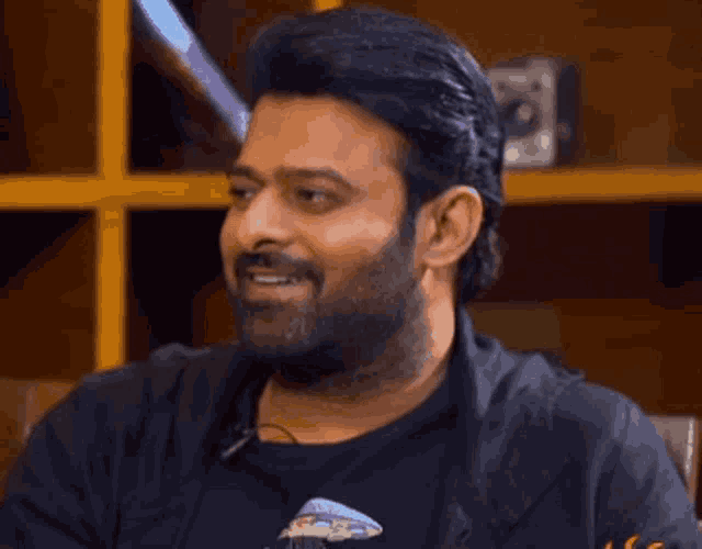 a man with a beard is smiling with his eyes closed while wearing a black shirt .