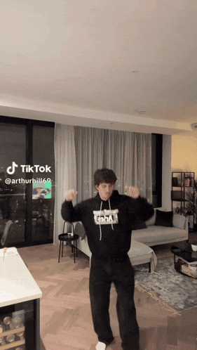 a man is dancing in a living room with a tiktok app on the wall