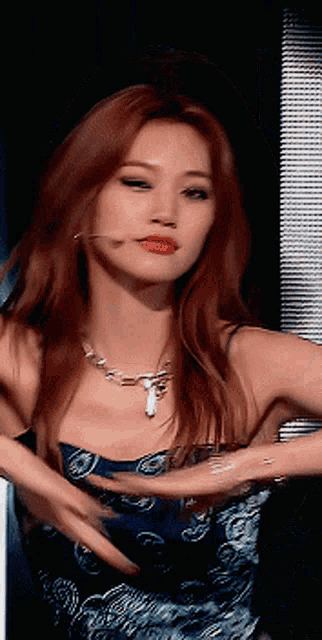 a woman with long red hair is wearing a blue dress and a necklace
