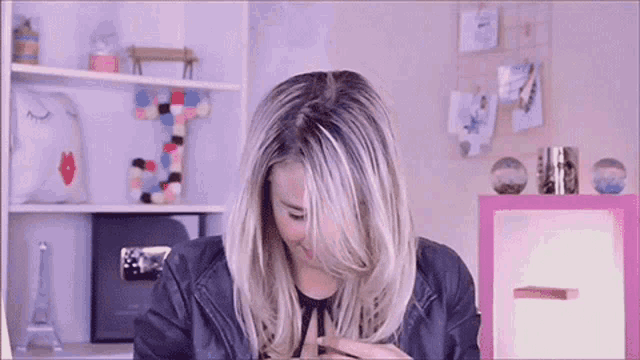 a woman wearing a leather jacket is sitting in front of a shelf with the letter j on it