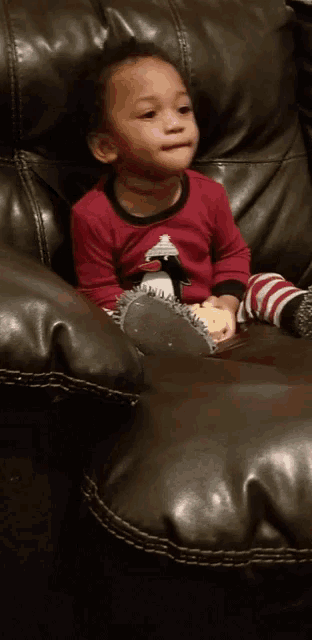 a little boy is sitting on a couch wearing a red shirt with a penguin on it
